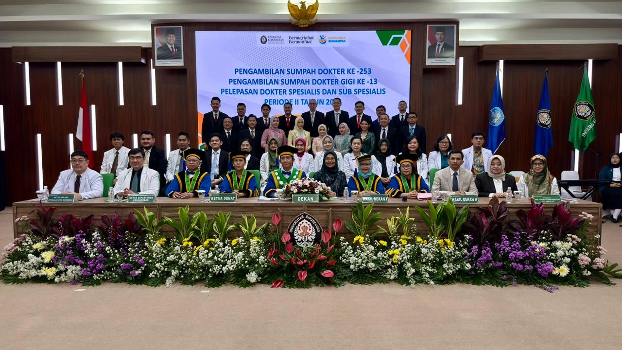 A group photo of the Universitas Diponegoro Faculty of Medicine leadership and graduates on stage, featuring a large digital backdrop for the April 2026 Medical Oath ceremony.